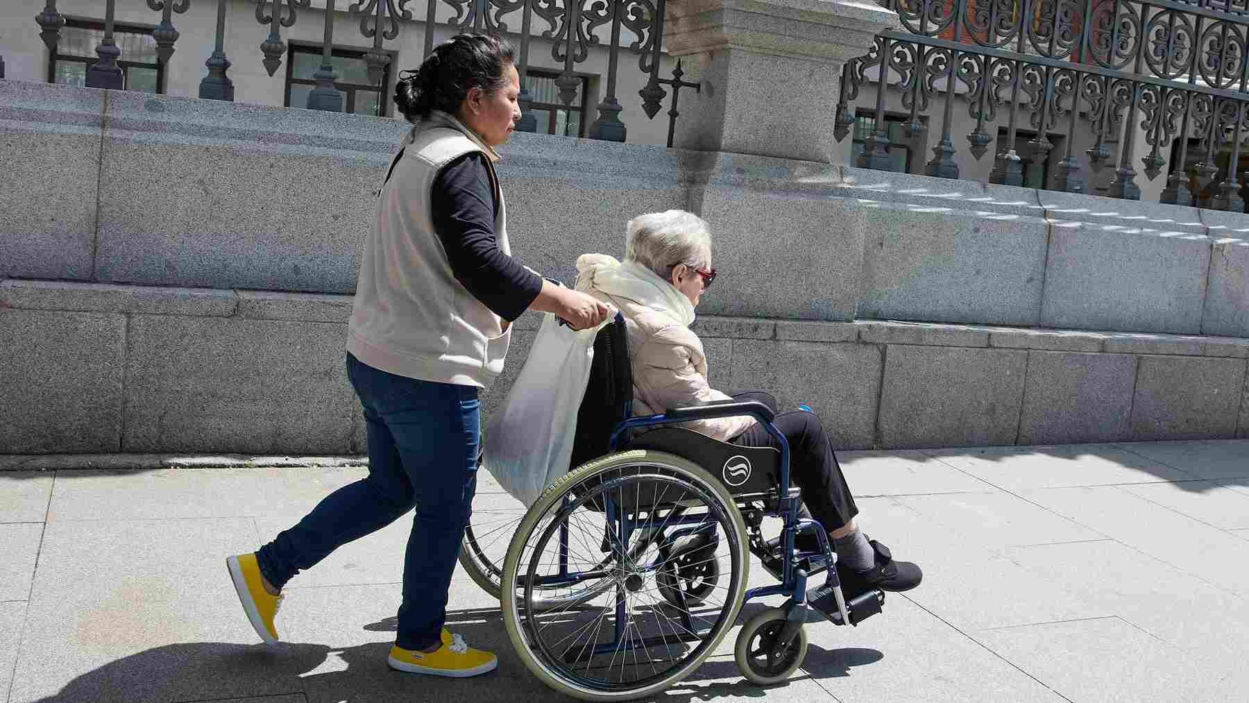 Una mujer mayor en silla de ruedas y su cuidadora. – Jesús Hellín – Europa Press –