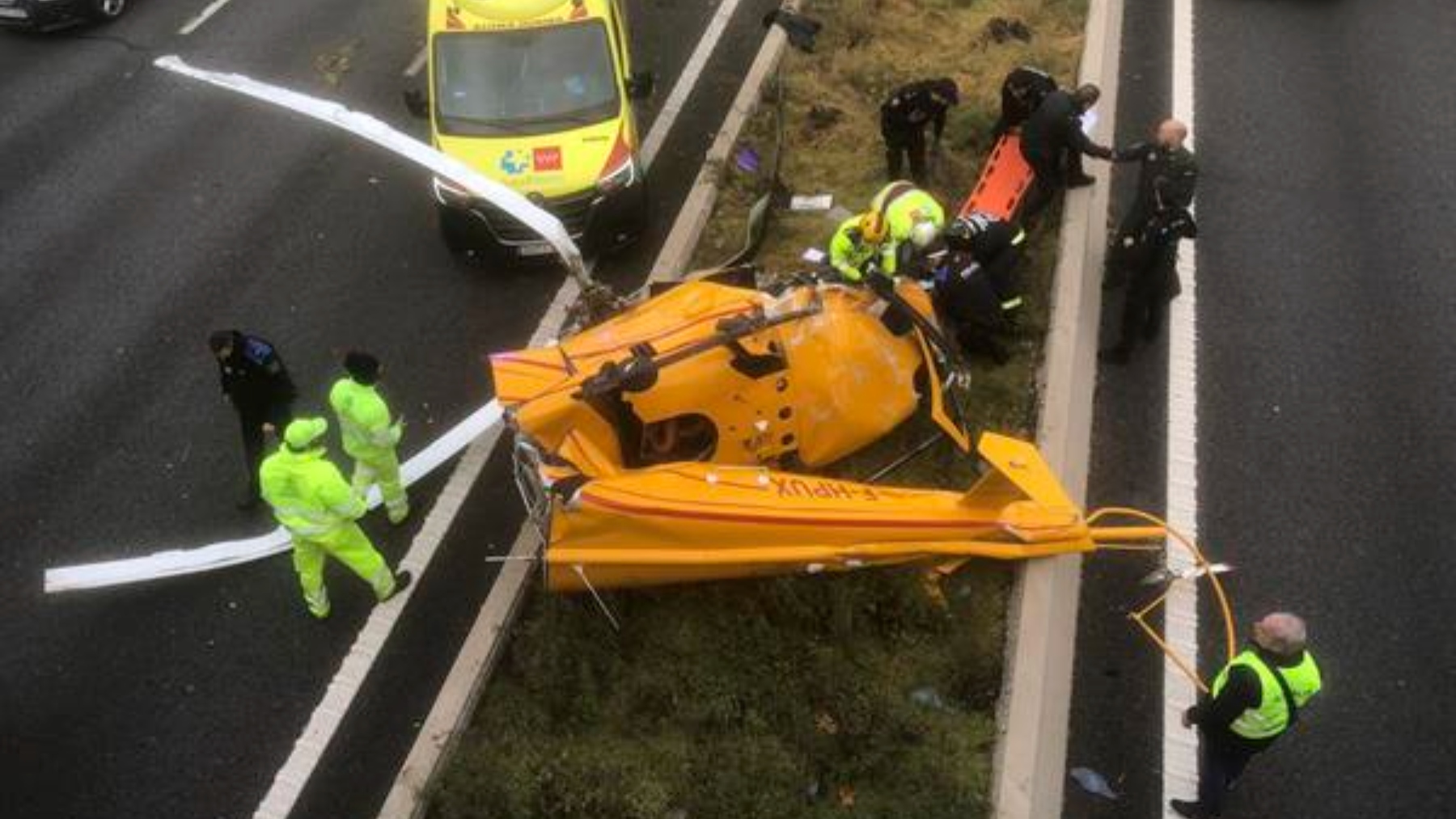 Los bomberos sacan a uno de los tripulantes heridos del interior del helicóptero accidentado en plena M40