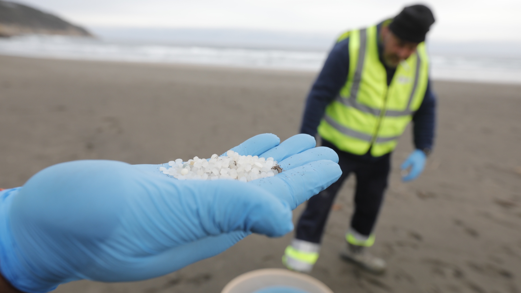 Un operario de TRAGSA coge con la mano pellets de plástico, en la playa Otur en Valdés, Asturias (Foto: Europa Press)