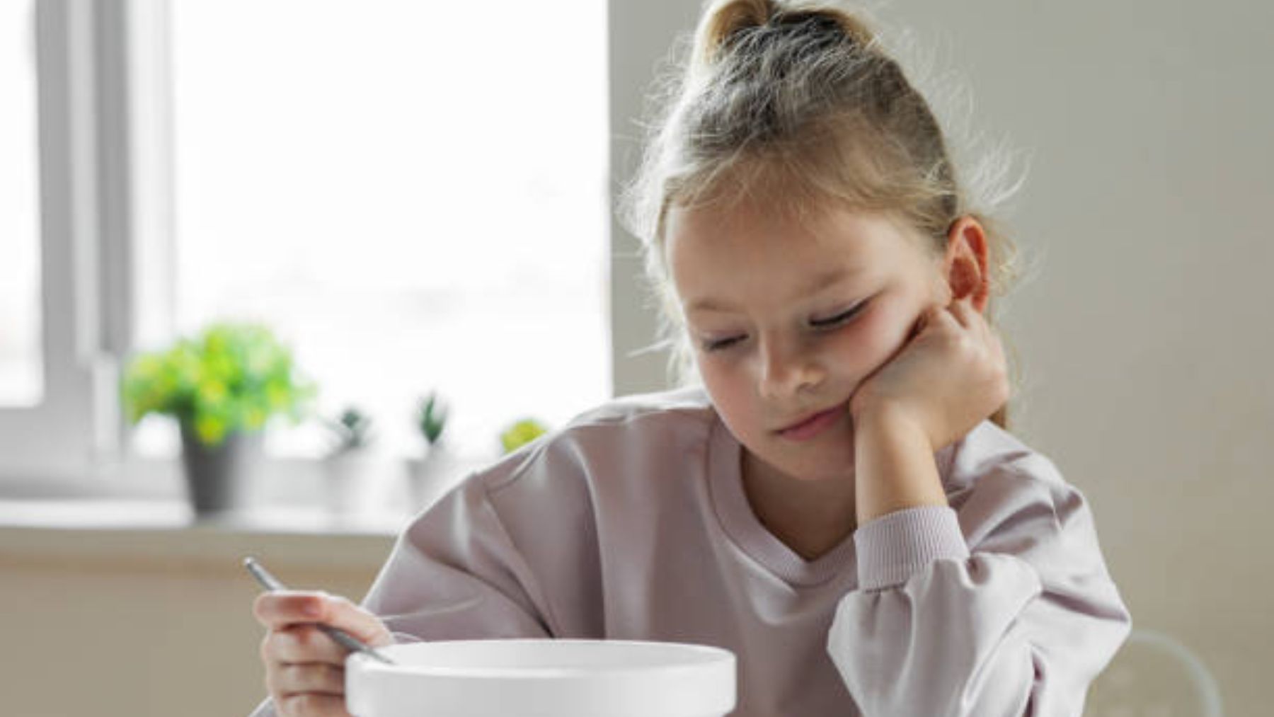 Niña sin ganas de come delante de su bol de comida.