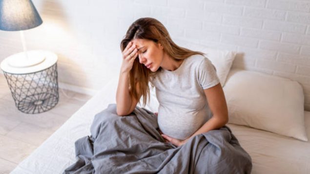 Mujer embarazada triste sentada en la cama.