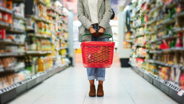 Mujer con cesta roja, en el pasillo de un supermercado.