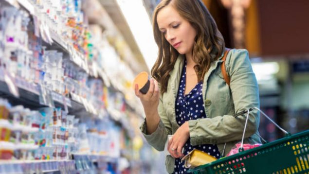 Mujer mirando un envase de un postre en un supermercado.