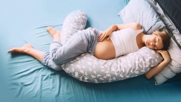 Foto de una embarazada durmiendo en la cama y con almohada de embarazo.