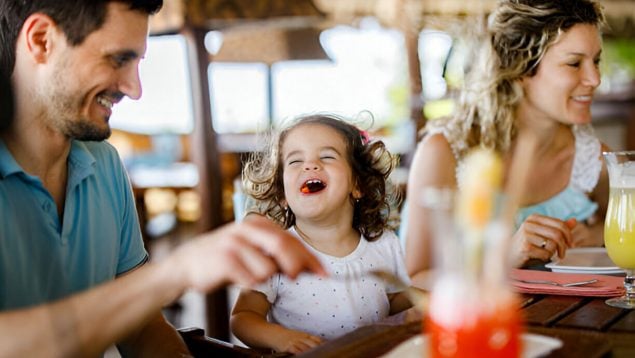Una familia de padre, madre y niña comiendo y riendo en un restaurante.