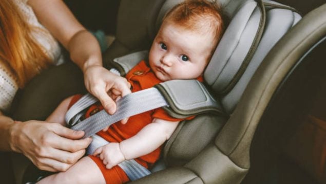 Sillita del coche del bebé con el bebé sentado y su padre que le abrocha.