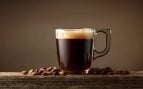 Taza de café de cristal con mucha crema y granos de café de fondo.