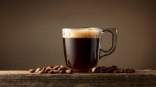 Taza de café de cristal con mucha crema y granos de café de fondo.