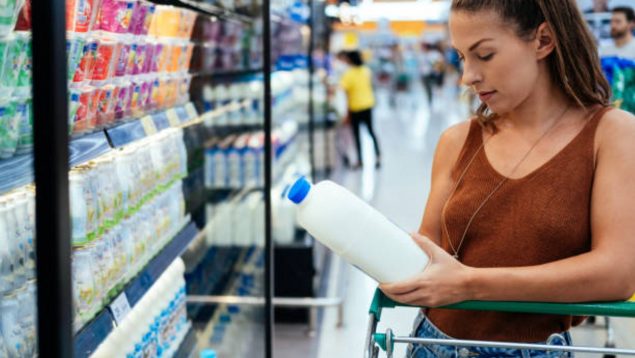 Una mujer compra leche en un supermercado y coge una botella con tapón azul.