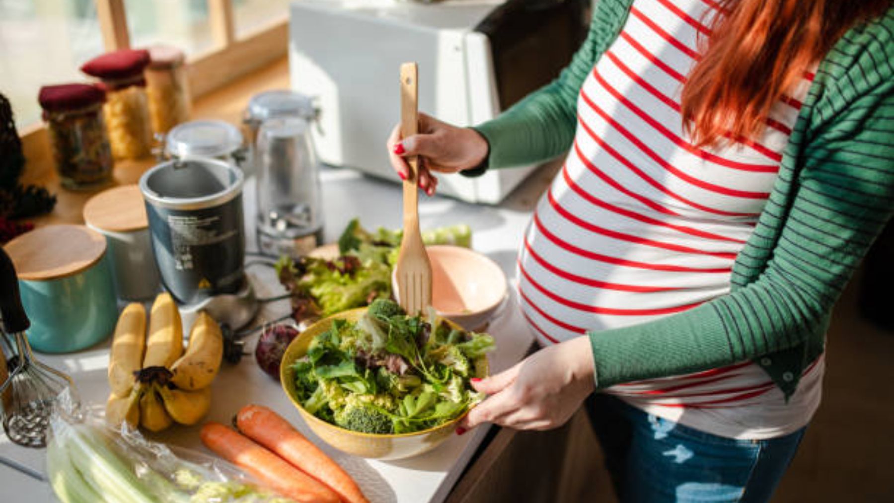 Mujer embarazada prepara ensalada.