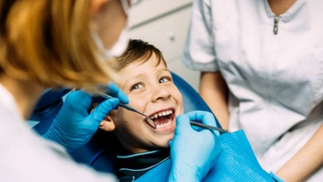 Foto de un niño en una revisión dental, con la doctora mirándole los dientes.