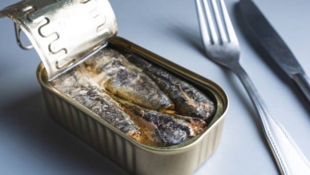 Foto de una lata de pescado en conserva abierta con aceite y con un tenedor al lado.