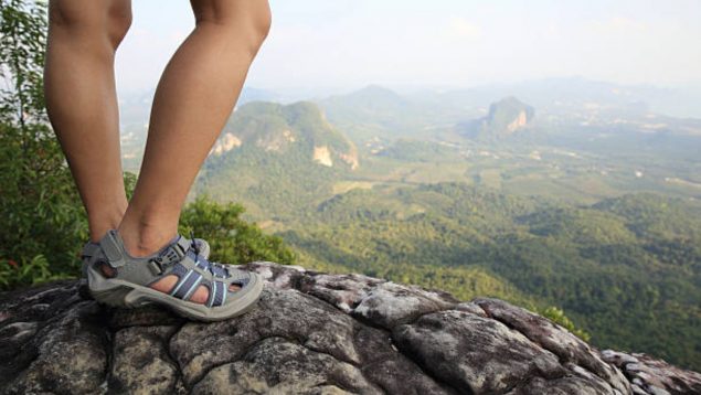 Una mujer sobre una piedra en el campo con unas sandalias de trekking.