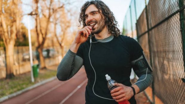 Foto de um hombre joven que come una barrita de chocolate después de entrenar.