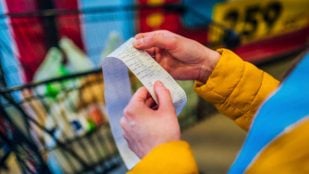 Manos de mujer sostienen ticket de compra en un supermercado.