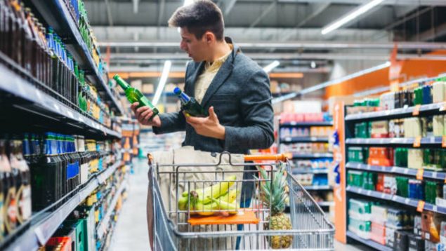 Hombre joven en un supermercado mirando dos botellas de cerveza.