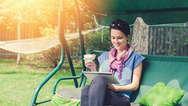 Mujer en un columpio de jardín mientras toma café y lee.