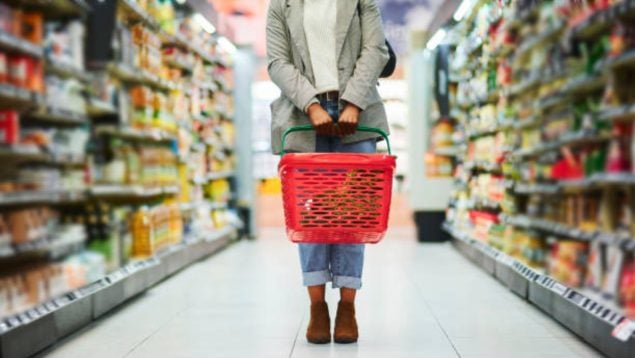Foto de una mujer en el centro de un supermercado con cesto rojo.