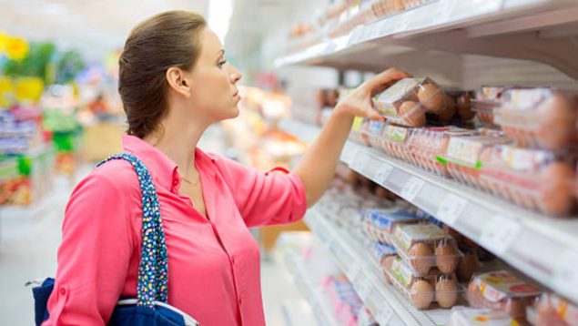 Foto de una mujer con blusa rosa cogiendo un cartón de huevos en un supermercado.