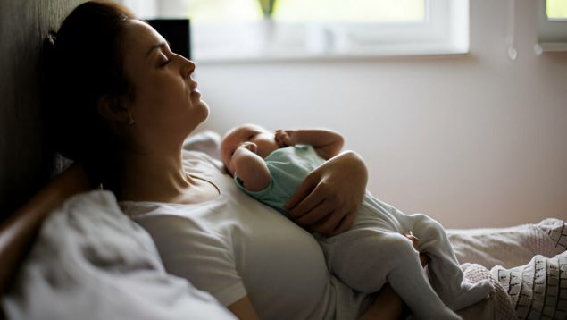 Mujer con su bebé sentada con expresión cansada