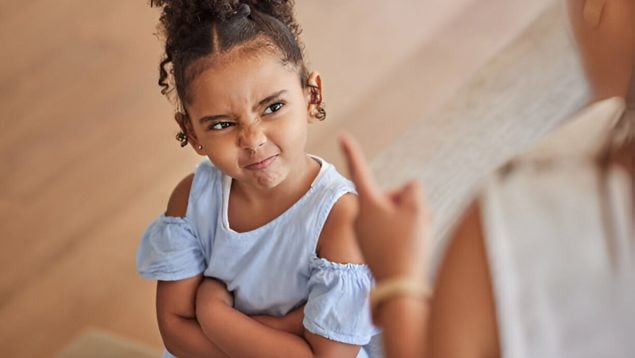 Foto de una niña frente a su madre. Está enfadada y de brazos cruzados.