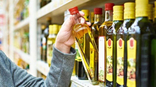 Foto de una mano cogiendo aceite de oliva en botella de cristal en un supermercado
