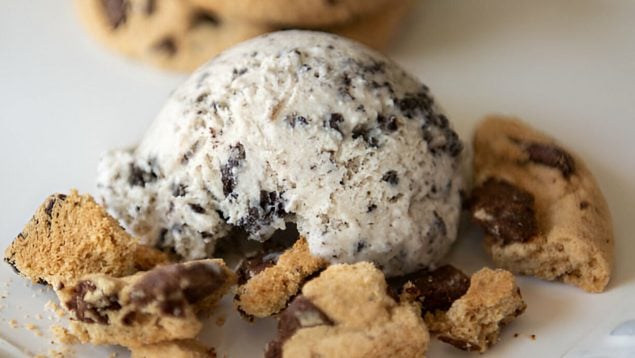 Foto de una bola de helado con trozos de chocolate y además con galleta.
