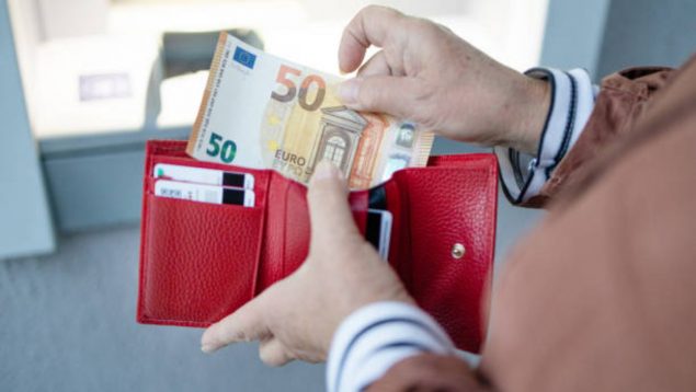 Foto de una cartera roja y como alguien mete dentro un billete de 50 euros.