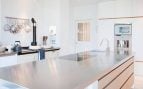 Foto de cocina con isla central de acero y madera y muebles en blanco con detalles de madera.