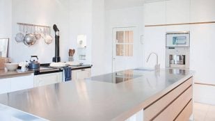 Foto de cocina con isla central de acero y madera y muebles en blanco con detalles de madera.