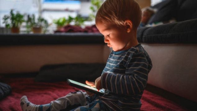 Foto de un niño pequeño en pijama iluminado por la luz de la pantalla de una tablet.