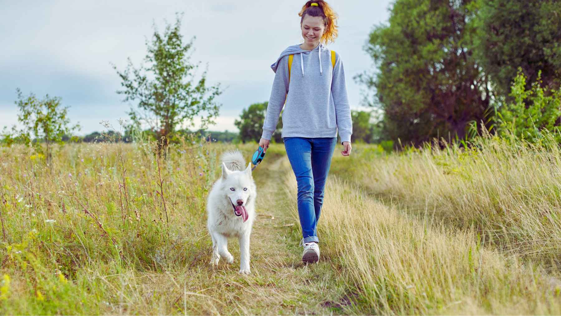 Una joven paseando con su perro por el campo.