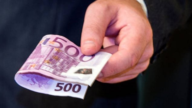 Foto de un hombre con traje, del que se ve sólo la mano y que tiene un billete de 500 euros doblado.