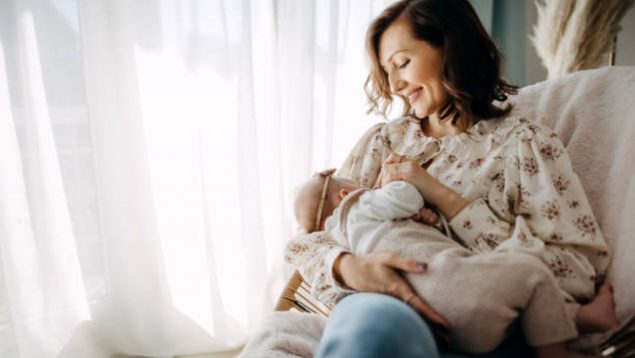 Foto de una madre sentada que sonriente mira a su bebé al que le da el pecho.
