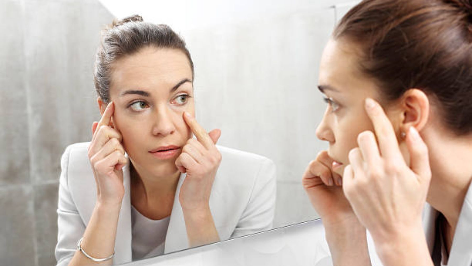 Mujer se mira las ojeras frente al espejo.