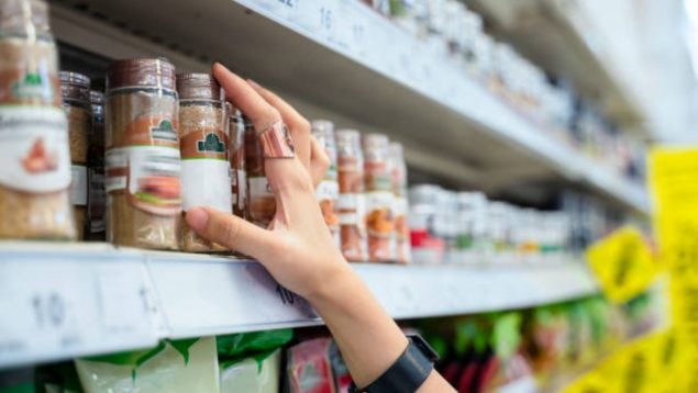 Foto de una mano que coge un bote de especias de la estantería de un supermercado.