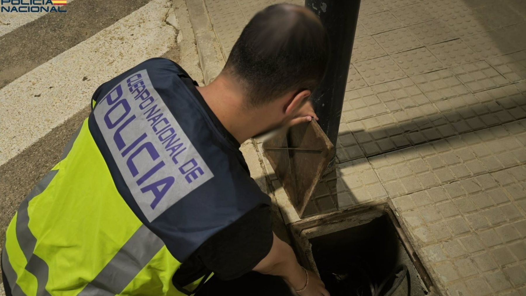 Un agente de la Policía Nacional junto a un poste de alumbrado público.