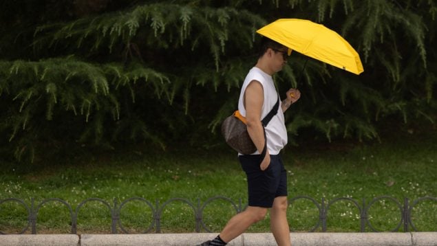 Un hombre se resguarda del sol bajo un paraguas.