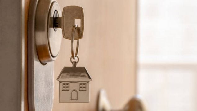 Foto de una puerta en cuyo cerrojo hay una llave con el llavero de una casa.