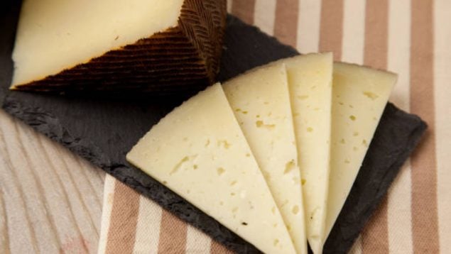 Foto de lonchas de queso cortadas sobre una tabla con la cuña al lado.