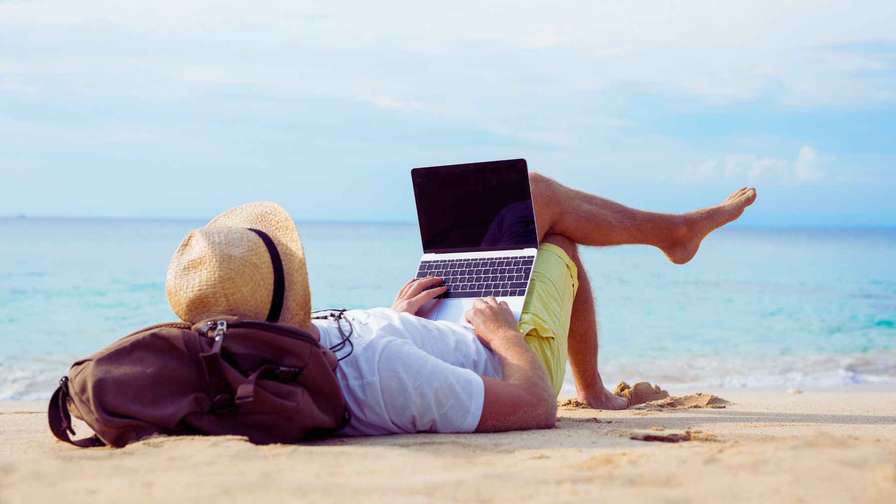 Un hombre con el ordenador portátil en la playa.