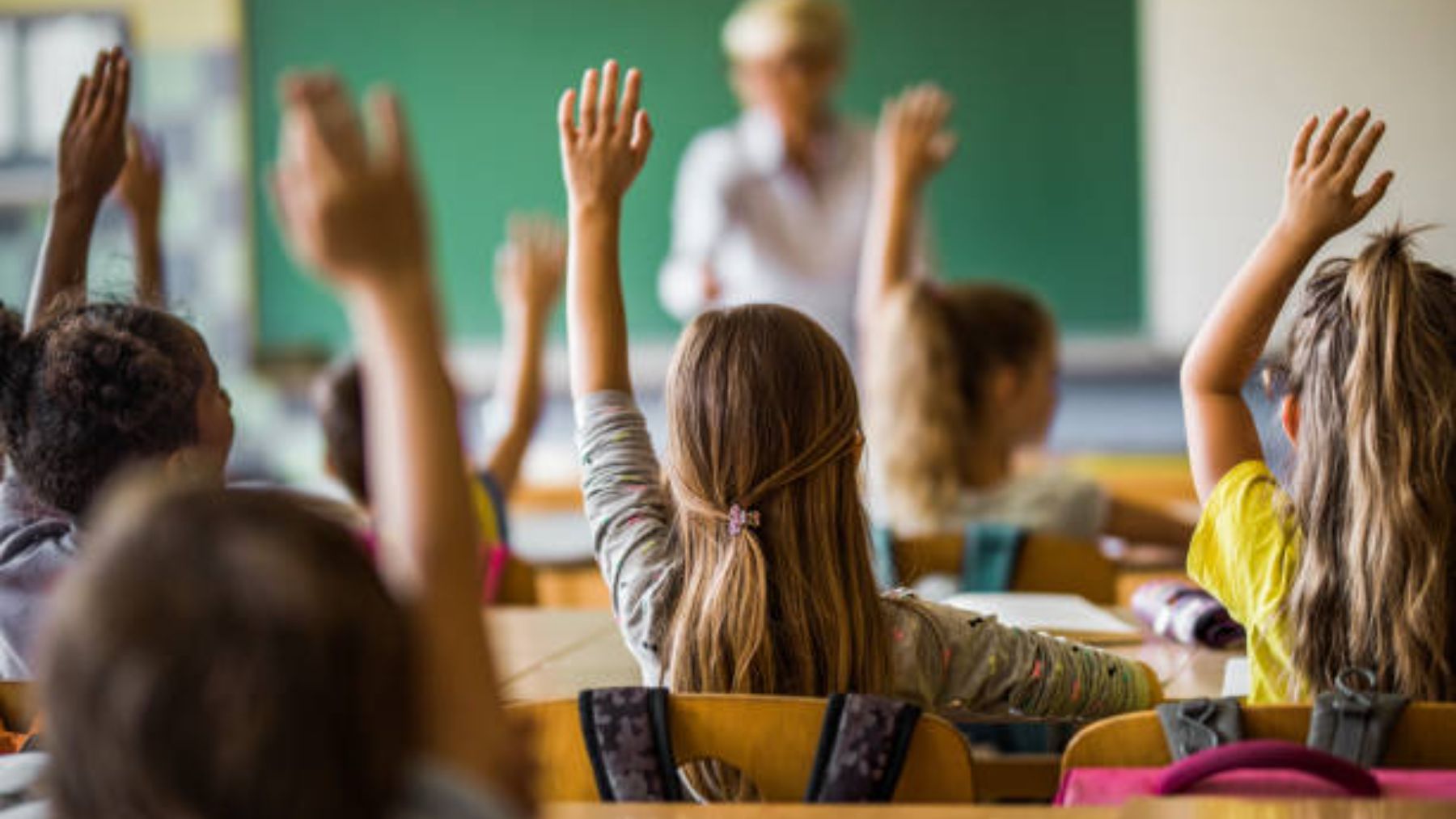 Niños en un aula levantando la mano.