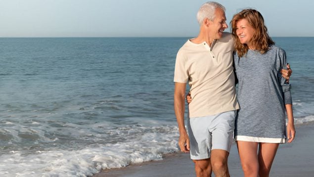 Foto de una pareja que camina que sonríe mientras camina por la orilla de la playa.