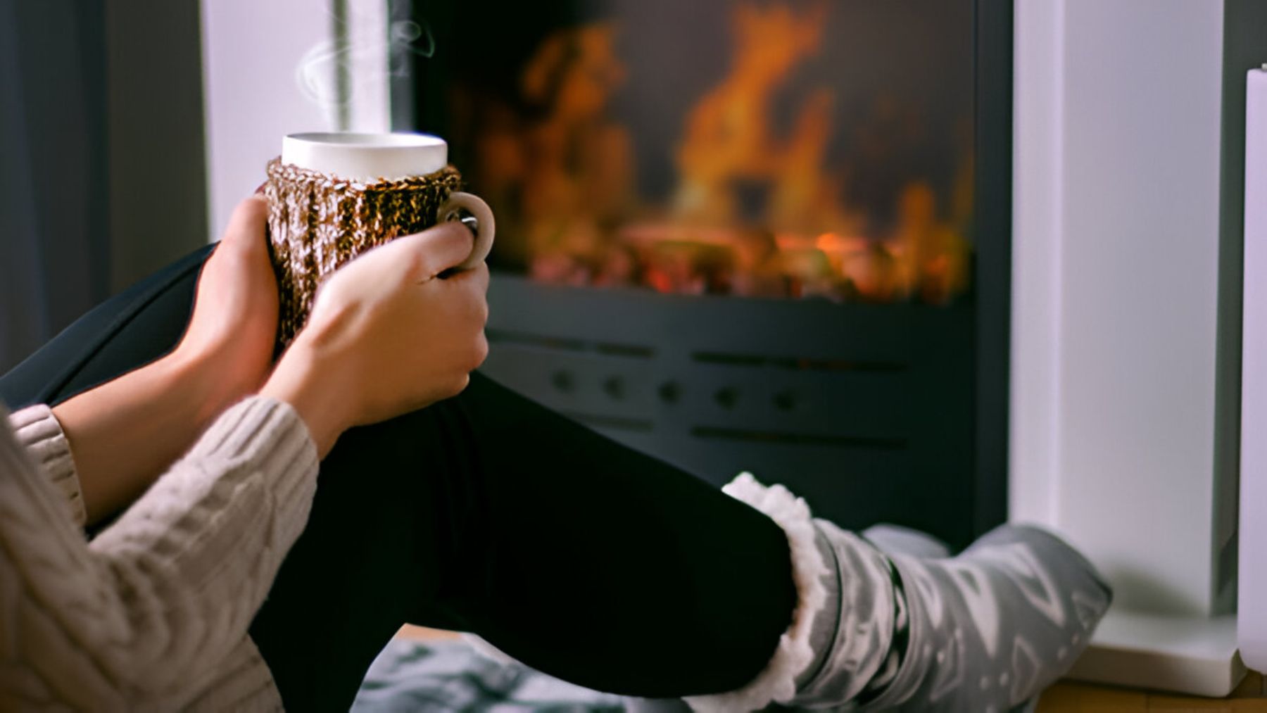 Mujer con taza caliente delante de su chimenea.