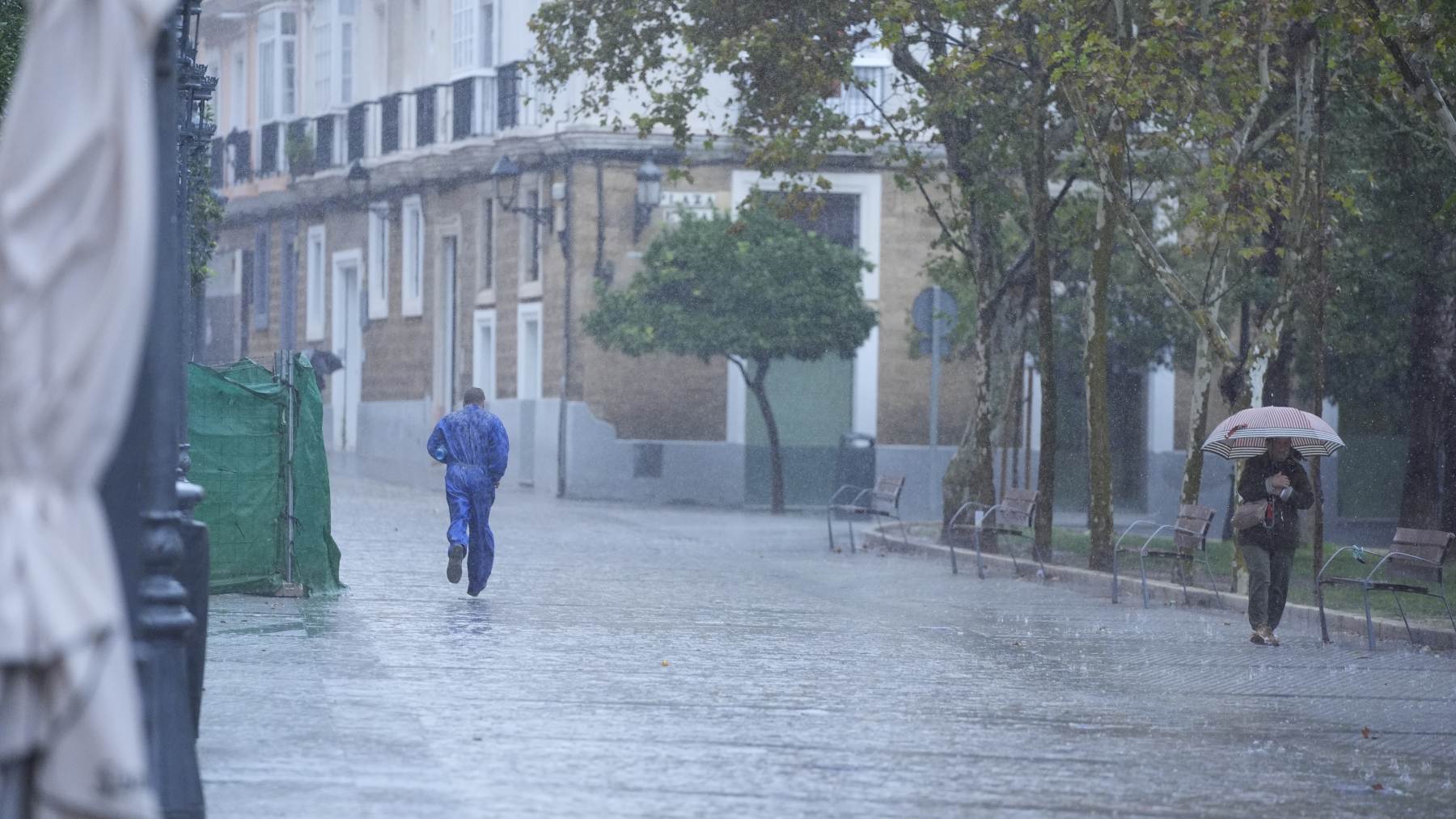 Gente corre bajo sus paraguas durante la intensa lluvia en Cádiz.