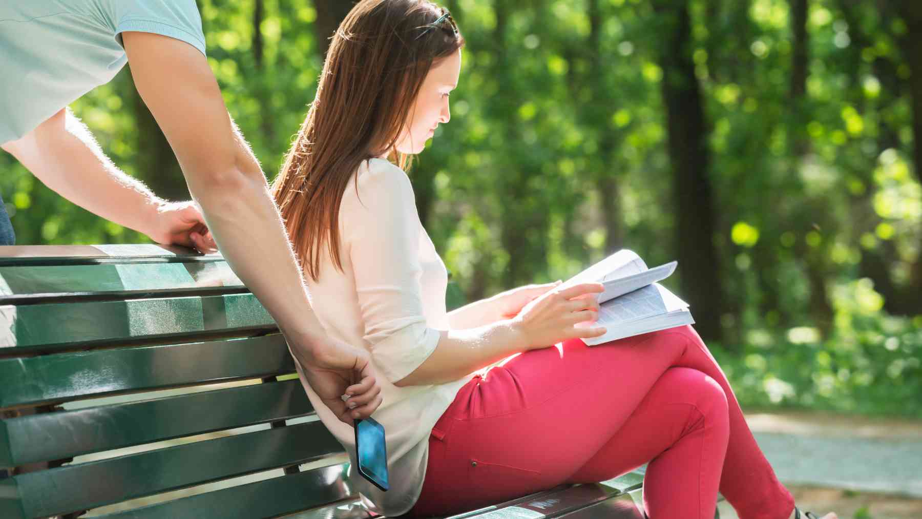 Alguien le roba el teléfono a una joven sentada en un parque.