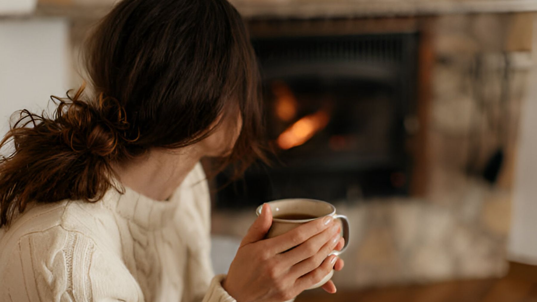 Mujer tomando café frente a la chimenea.