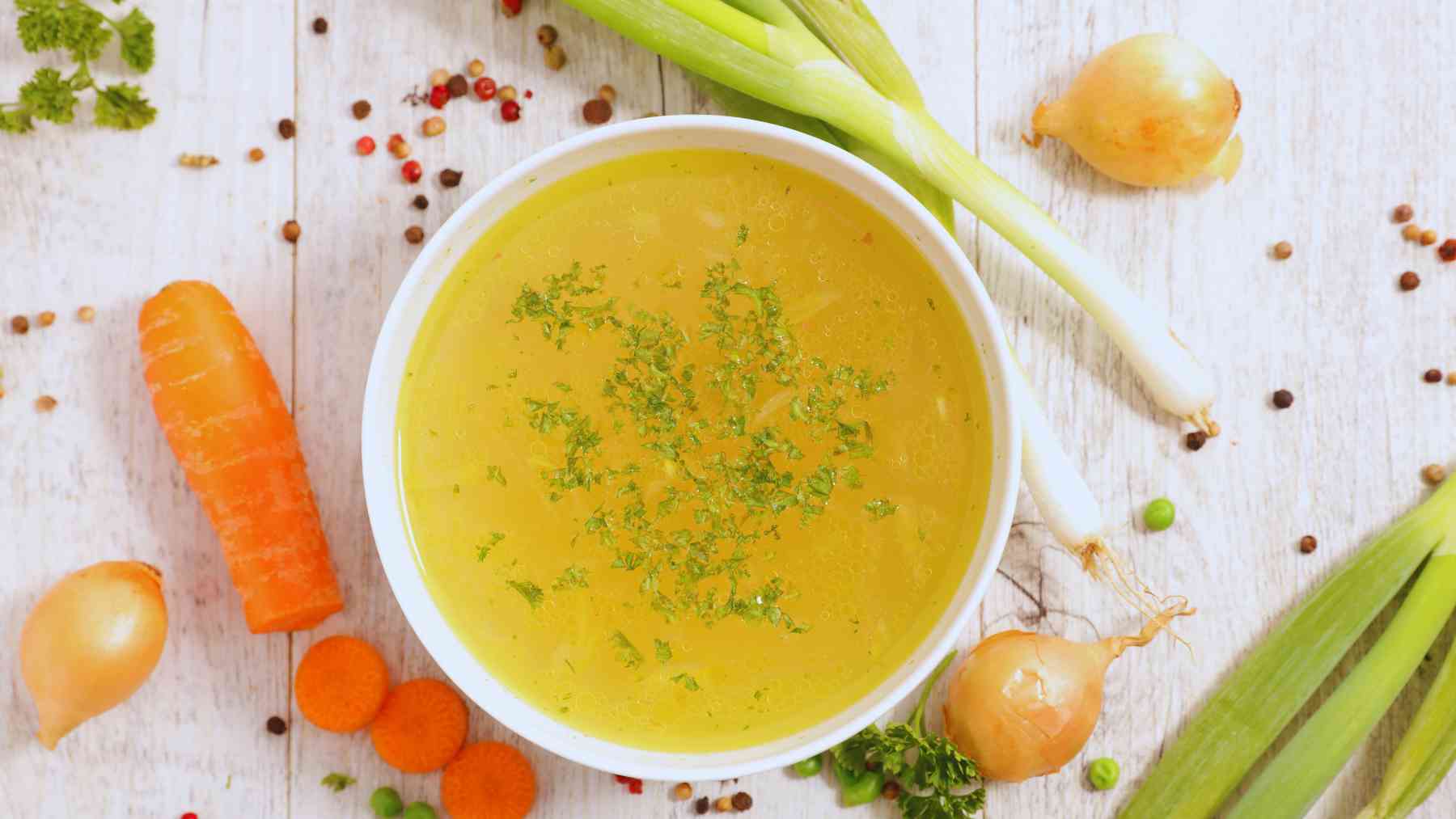 Un cuenco de caldo y varias verduras a su alrededor.