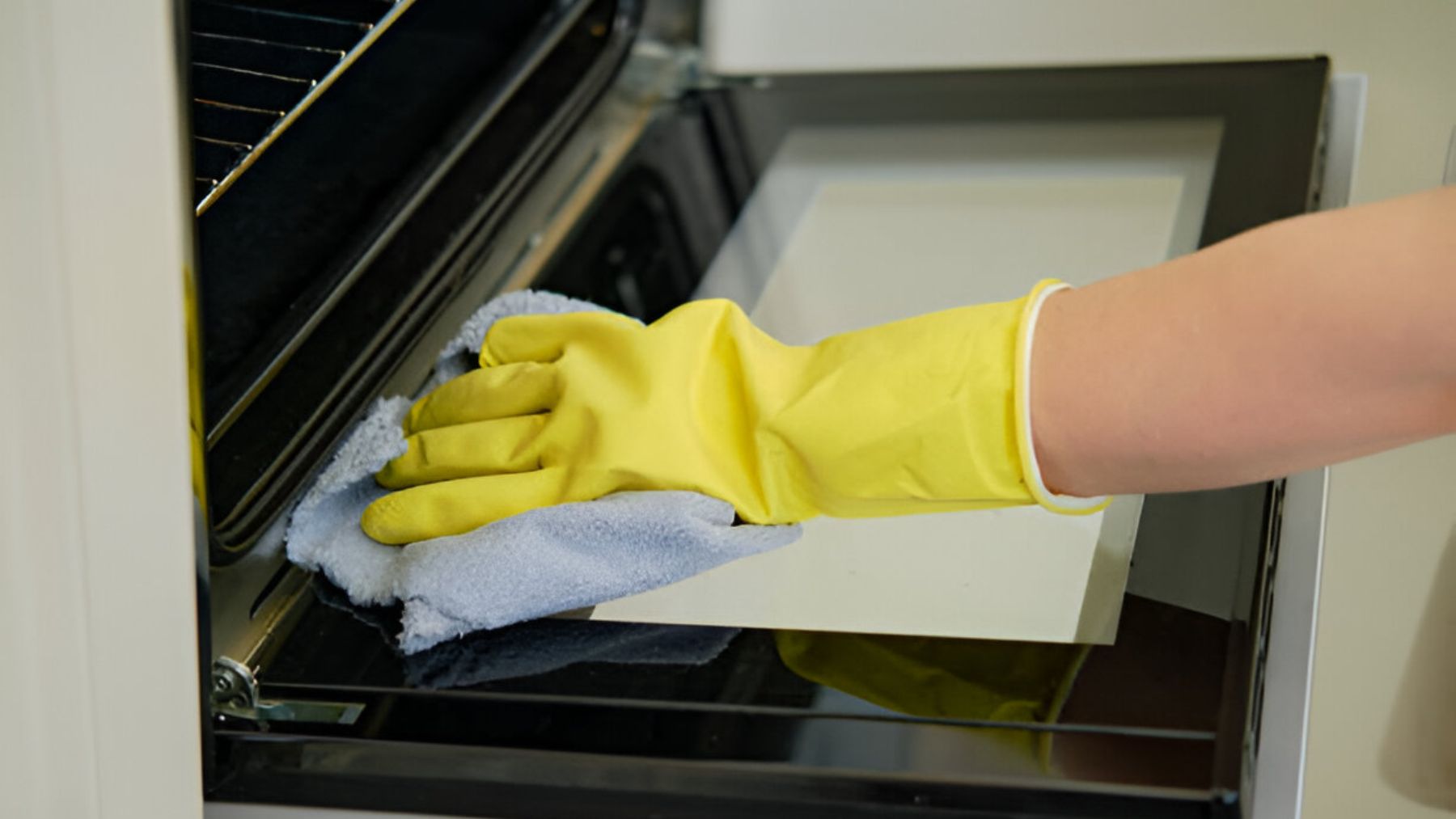 Mano con guante limpiando un horno.