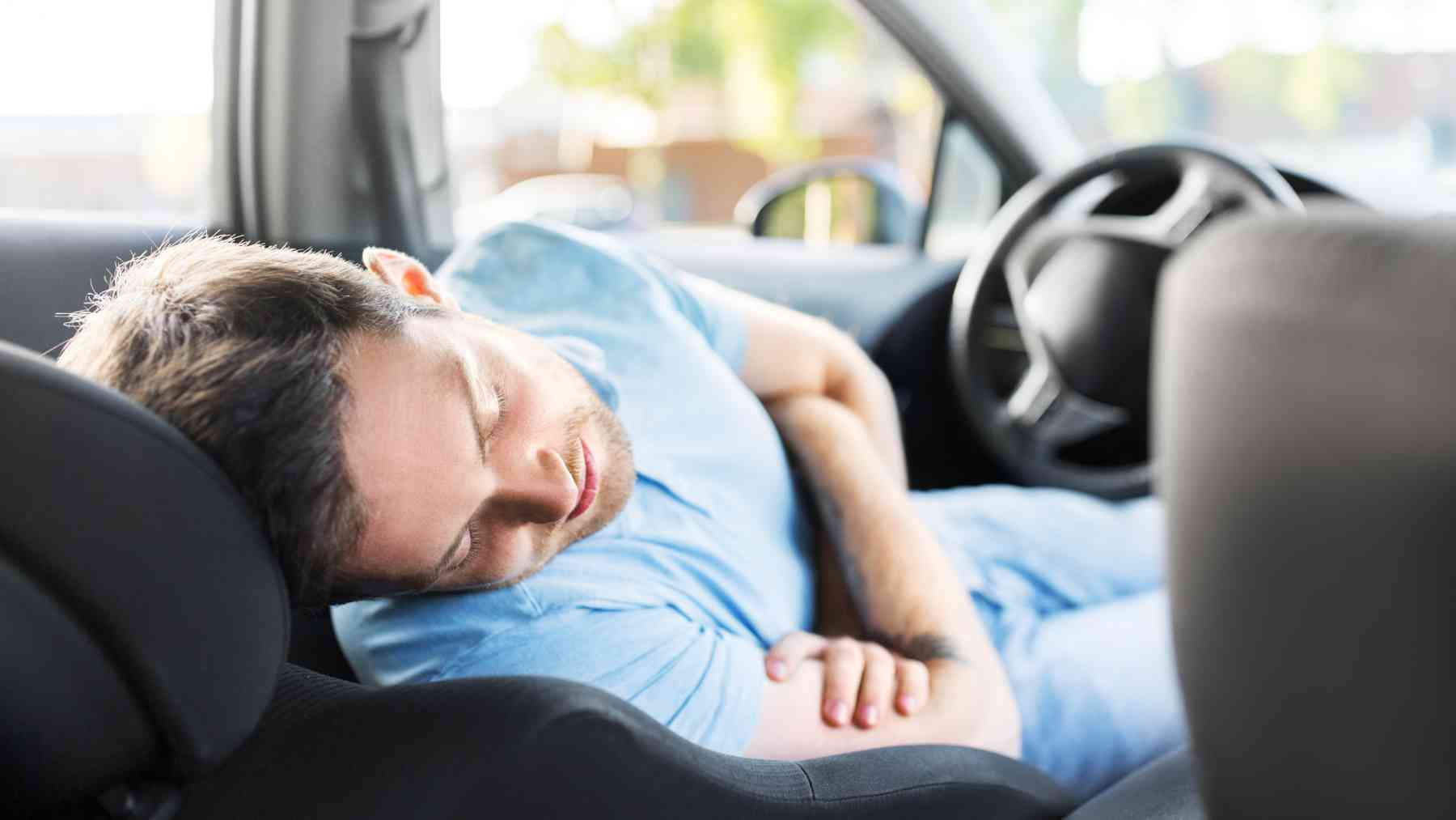 Un joven durmiendo en el coche.